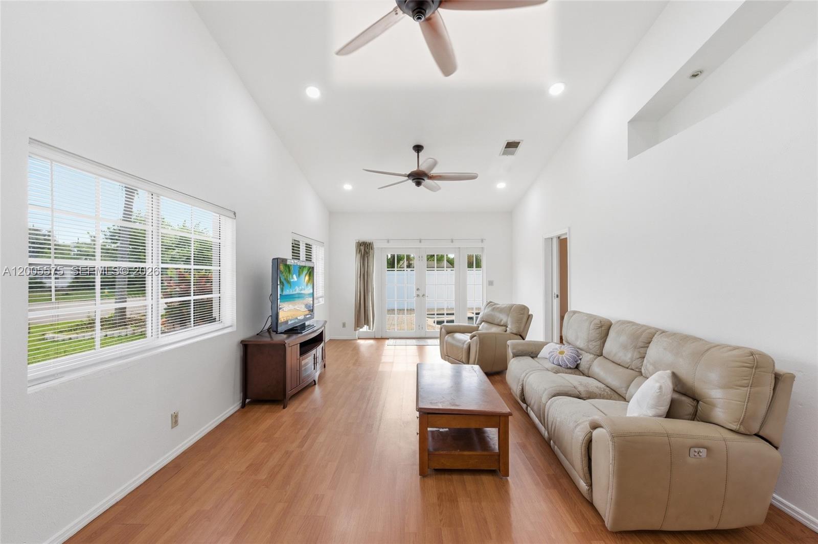 A living room features white walls, wood-look flooring, a vaulted ceiling, and a beige sofa — 4361 NE 13th Ter, Oakland Park FL 33334, OAKLAND PARK, FL