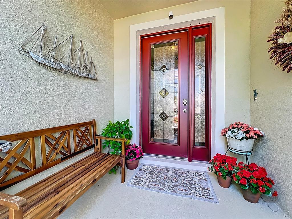 A front porch features a wooden bench, a red door with glass panels, and potted flowers — 15208 LAS OLAS PLACE, BRADENTON, FL