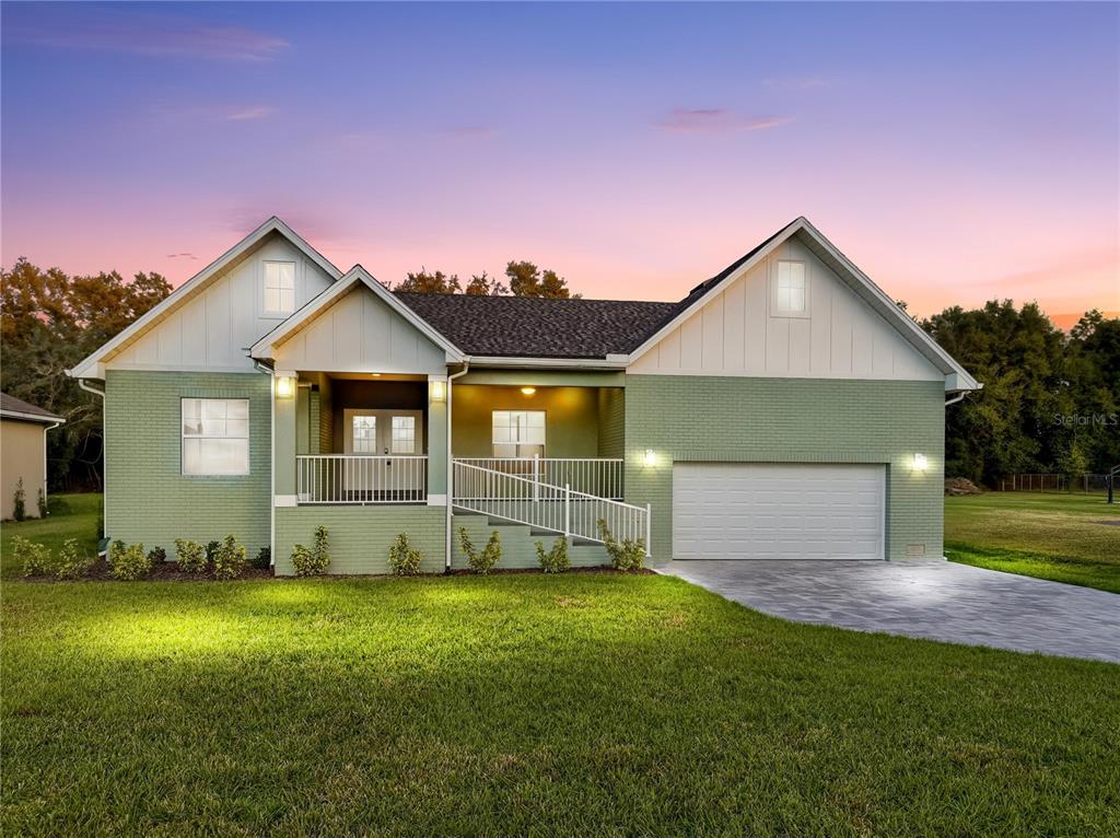 A light green brick house with a front porch, wheelchair ramp, and two-car garage — 12484 GREEN OAK LANE, DADE CITY, FL
