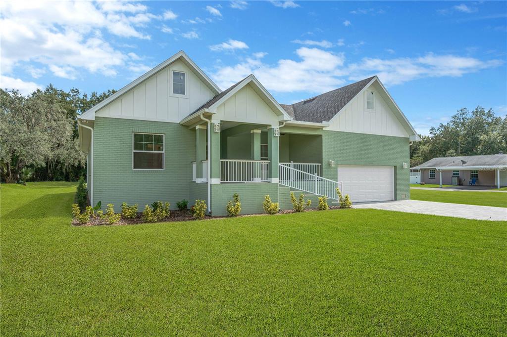 A green brick house with a covered front porch, white trim, and an attached garage — 12484 GREEN OAK LANE, DADE CITY, FL