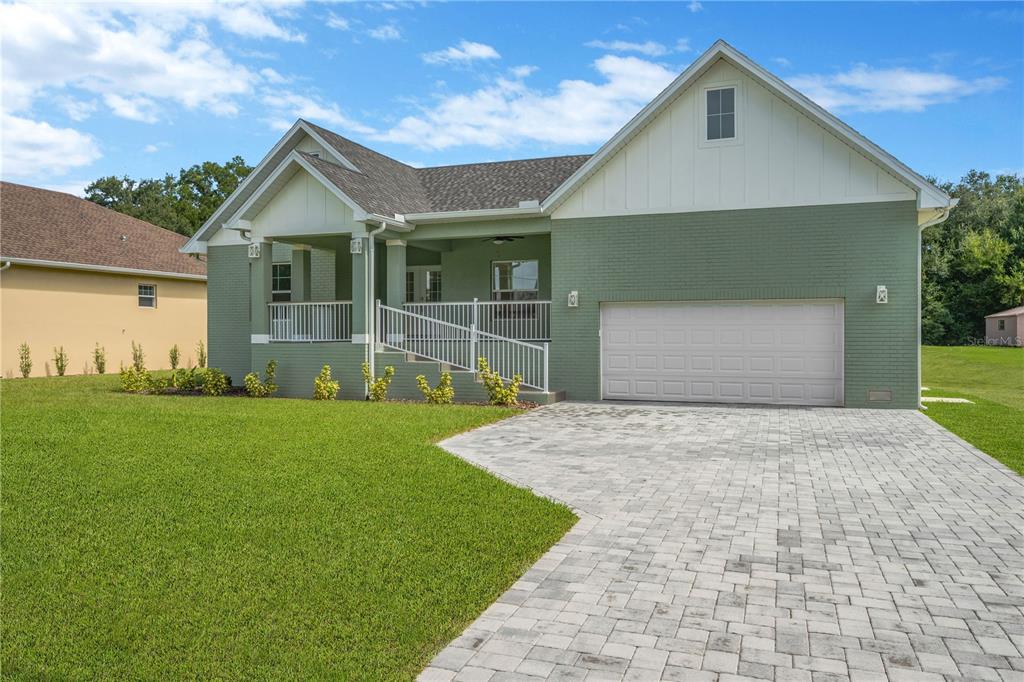 A green brick house with a white front porch, wheelchair ramp, and paved driveway — 12484 GREEN OAK LANE, DADE CITY, FL