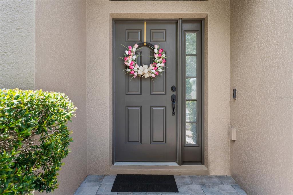A dark gray front door with a tulip wreath and a side window on a porch — 5716 RUE GALILEE LANE, SANFORD, FL