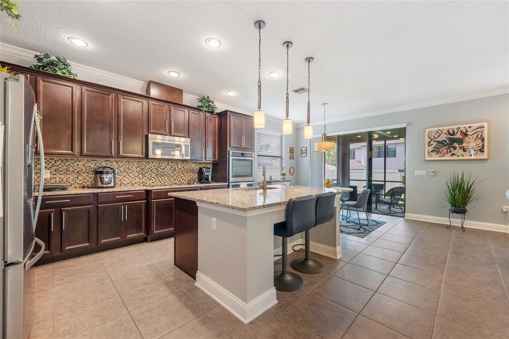 A kitchen with dark wood cabinets, granite countertops, a central island, and tile flooring — 5716 RUE GALILEE LANE, SANFORD, FL