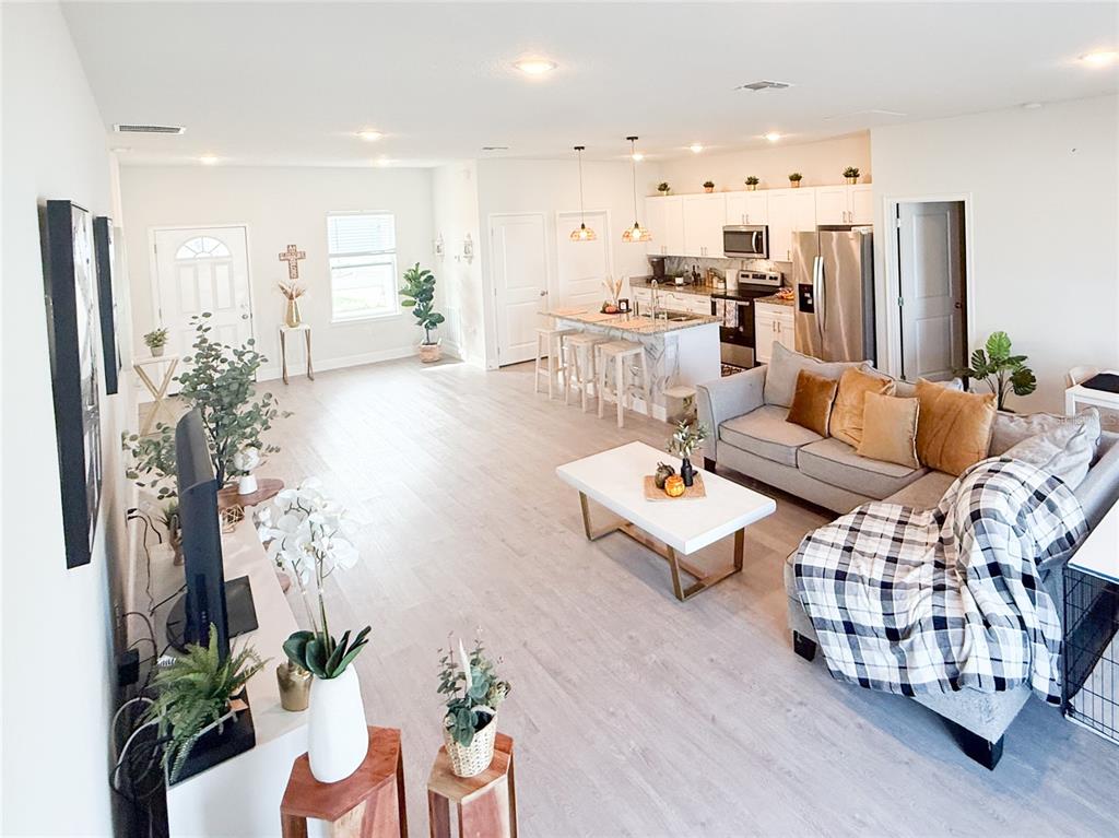 An open-concept living room and kitchen featuring light wood flooring and a gray sectional sofa — 25 ZINNIA LANE E, KISSIMMEE, FL