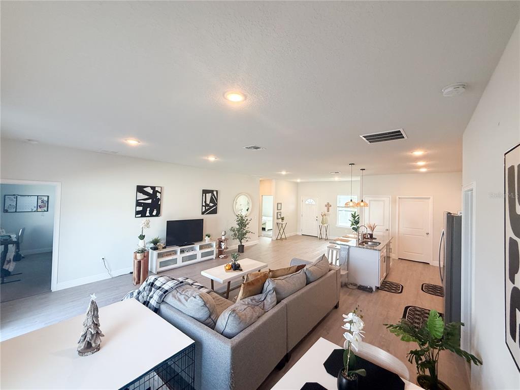 An open-concept living room and kitchen feature light wood flooring and a gray sectional sofa — 25 ZINNIA LANE E, KISSIMMEE, FL