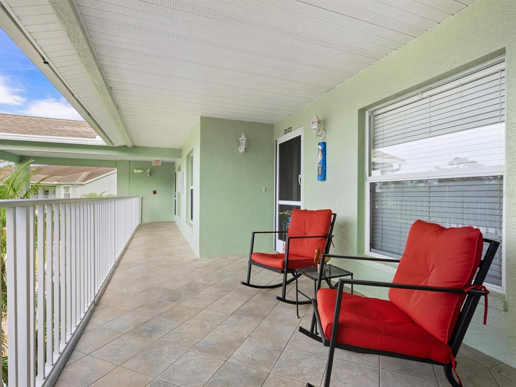 A covered balcony features tiled flooring, a white railing, and two red rocking chairs — 4645 TOWER HILL LANE UNIT 2522, SARASOTA, FL