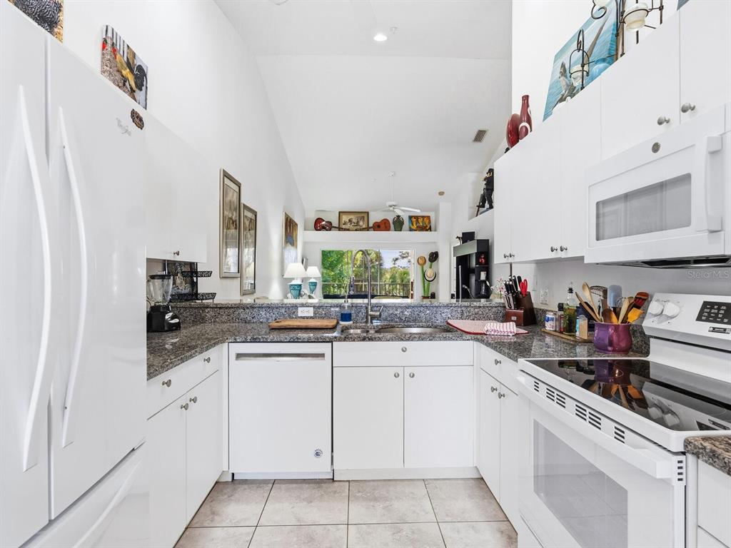 A white kitchen features granite countertops, white cabinetry, and stainless steel appliances — 4645 TOWER HILL LANE UNIT 2522, SARASOTA, FL