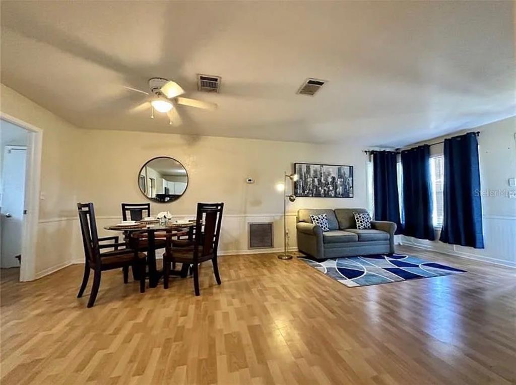 A dining area and living room feature hardwood floors, a ceiling fan, and blue curtains — 7523 MAYLAND STREET, NORTH PORT, FL