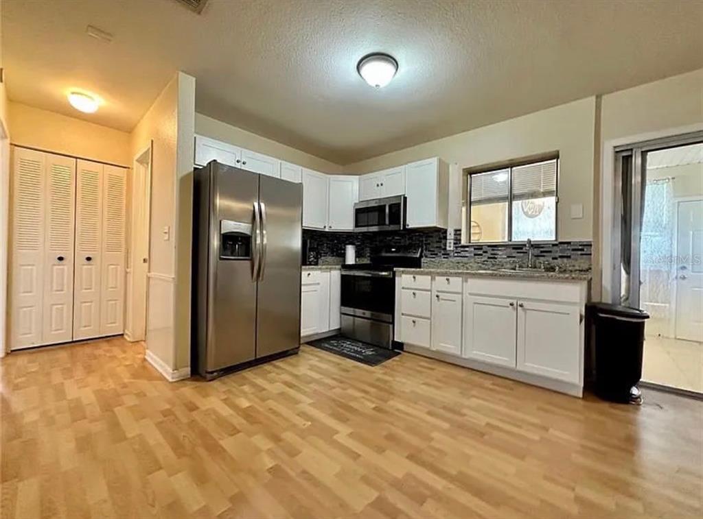 A kitchen features white cabinets, stainless steel appliances, a tiled backsplash, and light wood flooring — 7523 MAYLAND STREET, NORTH PORT, FL