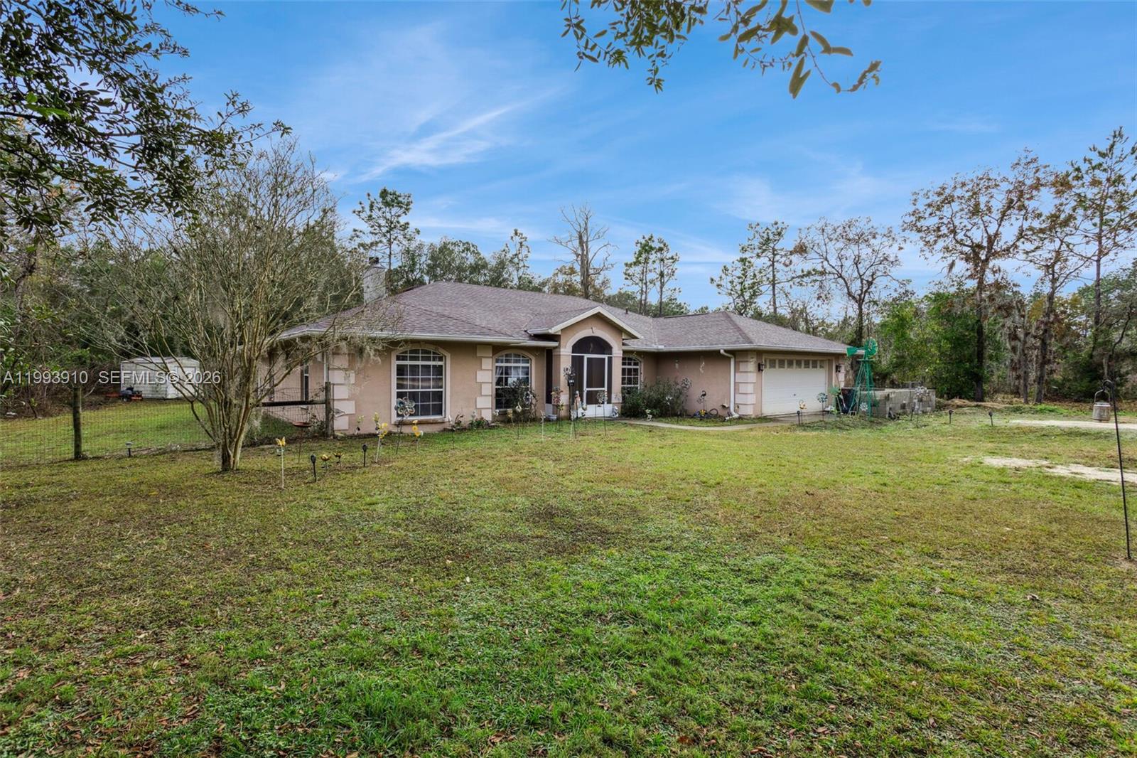 A single-story tan house with a white garage and arched windows sits on a lawn — 14170 SE 4th St., Williston FL 32696, WILLISTON, FL