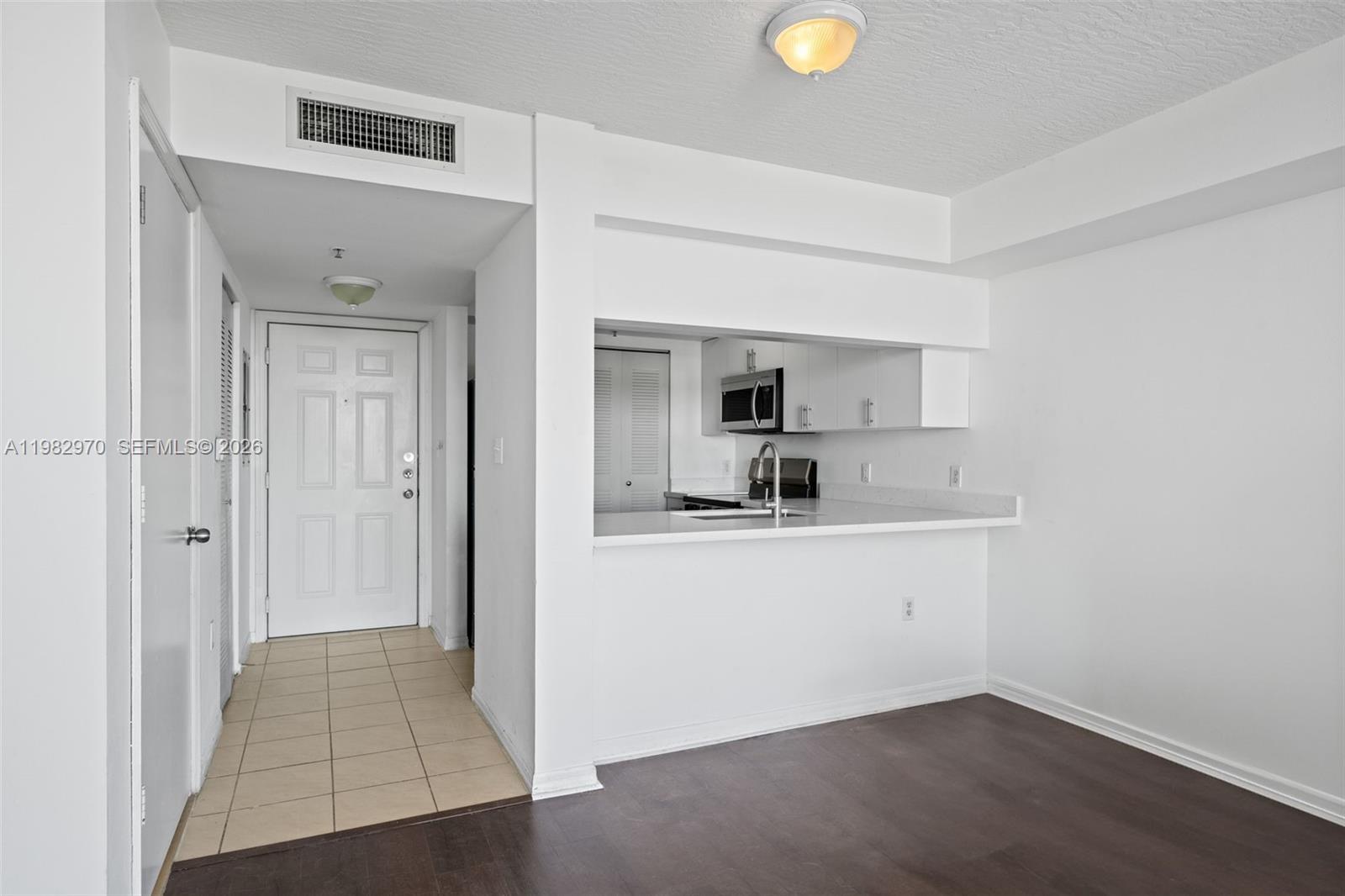 A kitchen with white cabinets and a breakfast bar overlooks a room with flooring — 102 SW 6th Ave # 605, Miami FL 33130, MIAMI, FL