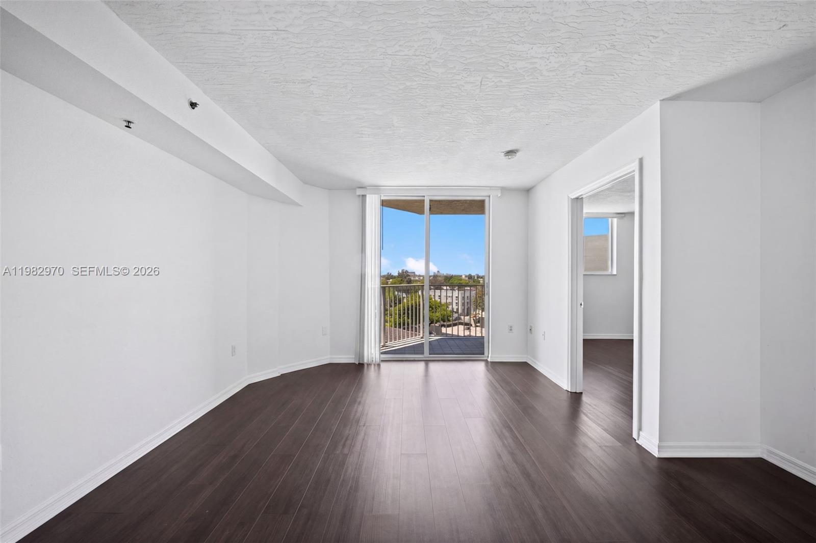 An empty living room features dark wood flooring, white walls, and a sliding glass door — 102 SW 6th Ave # 605, Miami FL 33130, MIAMI, FL