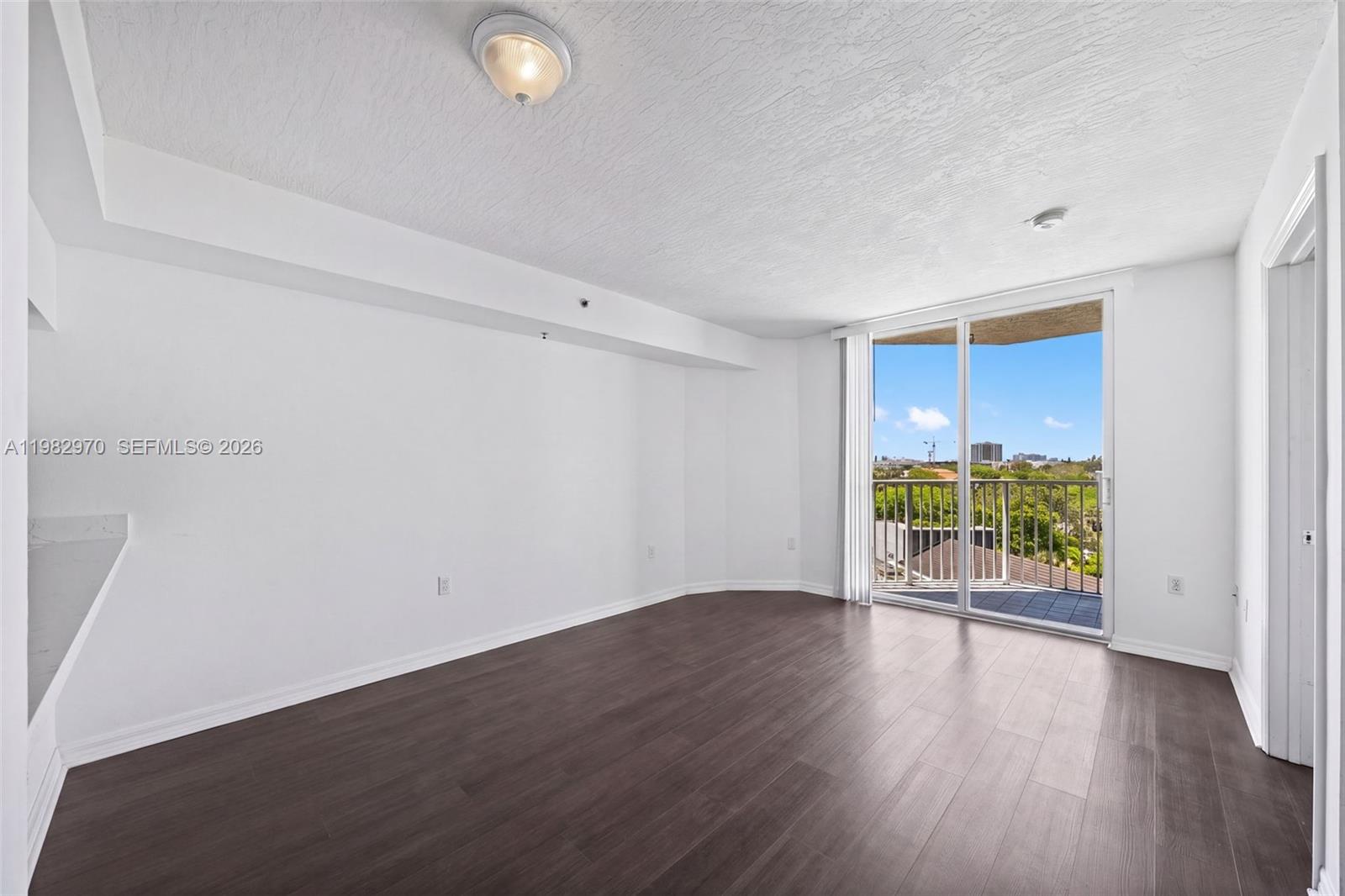 An empty room features white walls, dark wood-look flooring, and a sliding glass door to a balcony — 102 SW 6th Ave # 605, Miami FL 33130, MIAMI, FL