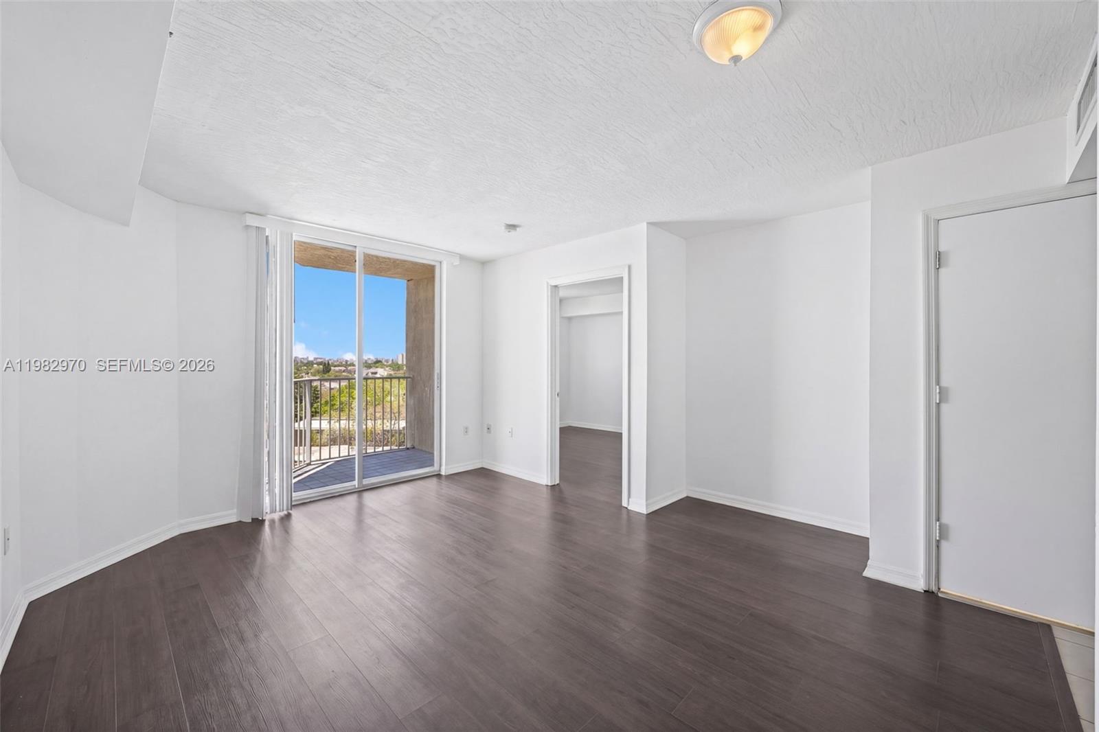 An empty room with dark wood-look flooring, white walls, and a sliding glass balcony door — 102 SW 6th Ave # 605, Miami FL 33130, MIAMI, FL