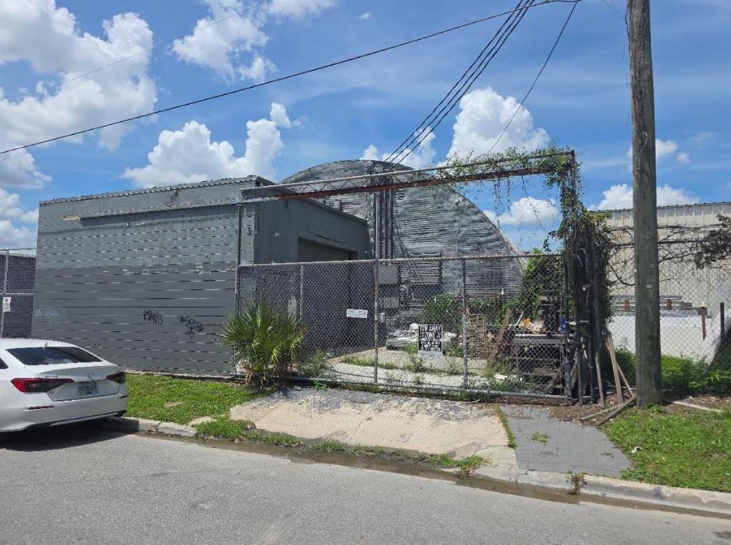 A fenced-in industrial lot features a grey building with a curved roof and graffiti — 1001 W PINE STREET, ORLANDO, FL