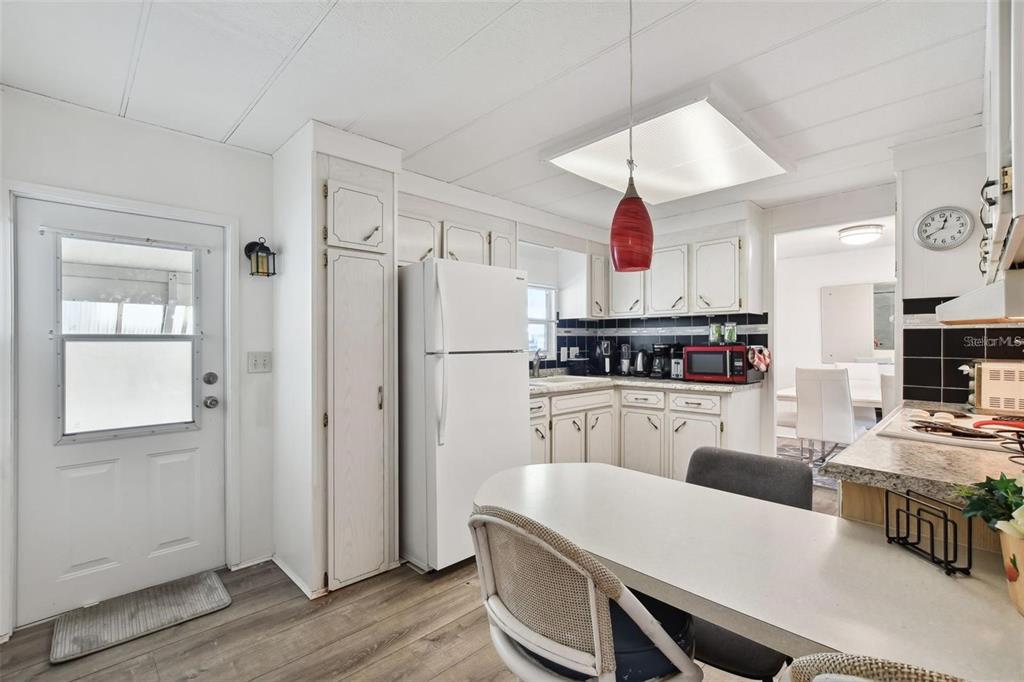 A white kitchen features a dining table, a red pendant light, and wood-look flooring — 13225 101ST STREET UNIT 116, LARGO, FL