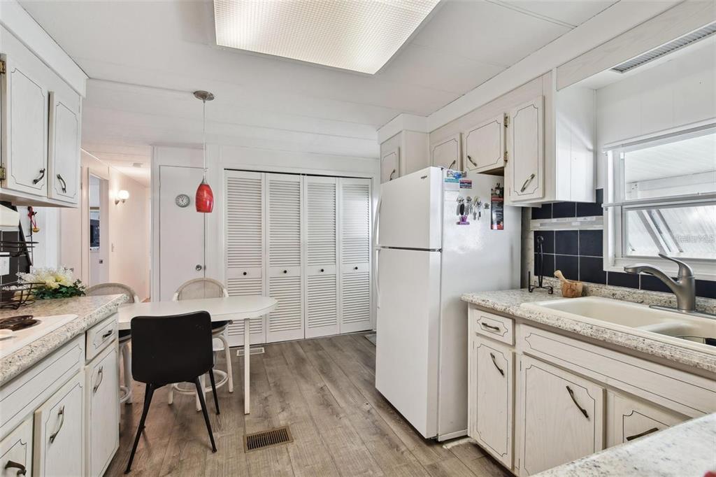 A kitchen features white cabinetry, a white refrigerator, a small dining table, and wood-look flooring — 13225 101ST STREET UNIT 116, LARGO, FL