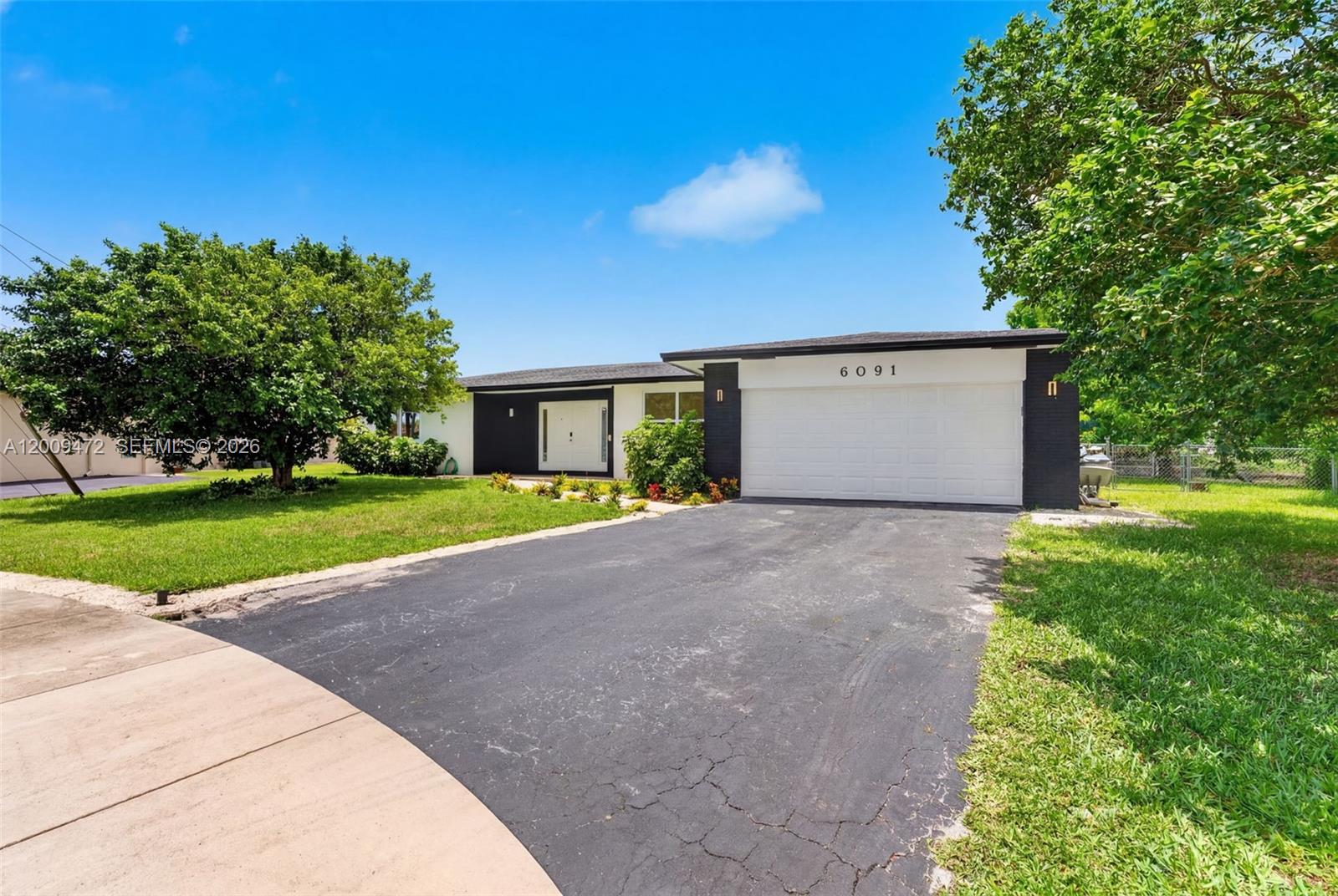 A single-story house with a white garage, black accents, and a paved driveway — 6091 SW 14th St, Plantation FL 33317, PLANTATION, FL