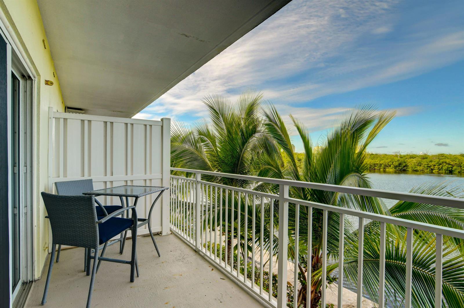 A balcony with a small table and two chairs overlooking palm trees and a lake — 6520 N Ocean Boulevard # 24, Ocean Ridge FL 33435, OCEAN RIDGE, FL