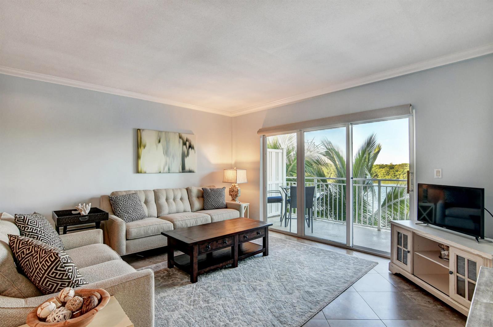 A living room features a beige sofa, wooden coffee table, television, and a balcony with water views — 6520 N Ocean Boulevard # 24, Ocean Ridge FL 33435, OCEAN RIDGE, FL