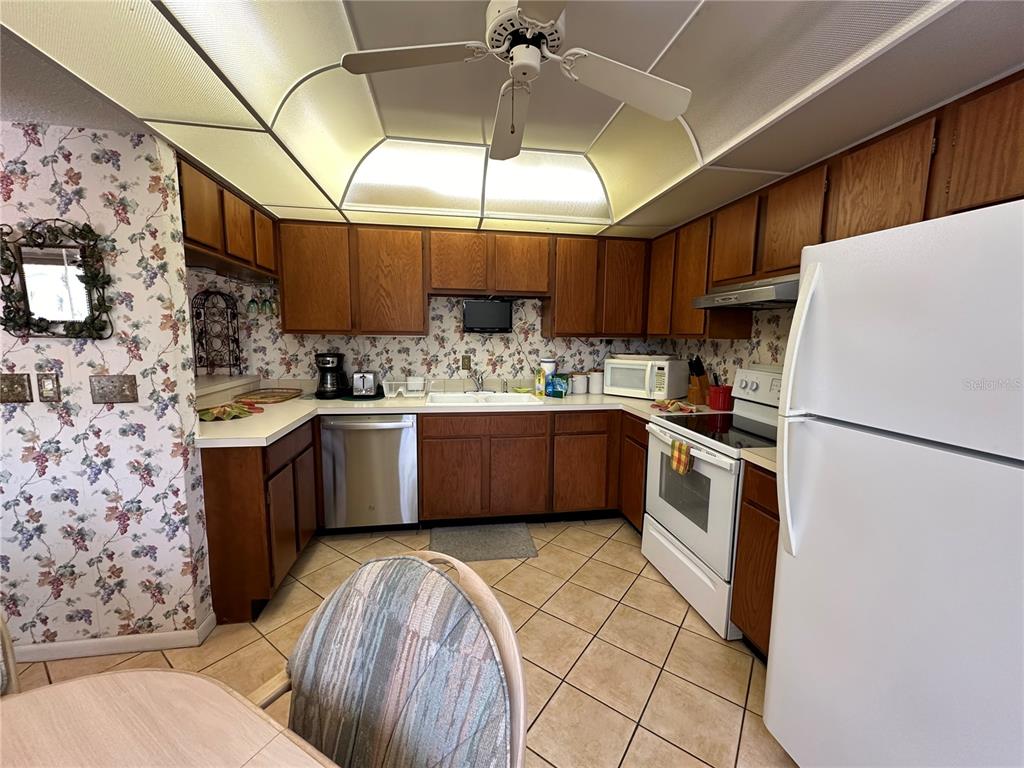 A kitchen with wood cabinets, floral wallpaper, tile flooring, and a white refrigerator — 1647 BROOKHOUSE COURT UNIT 246, SARASOTA, FL