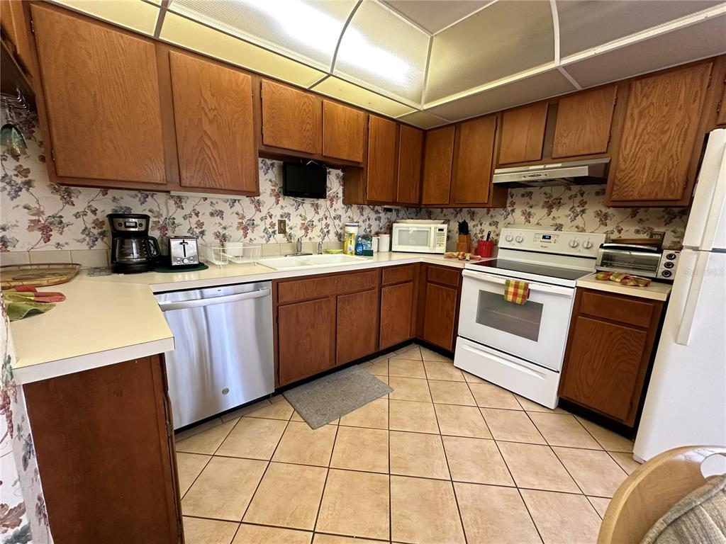 A kitchen features wood cabinets, floral wallpaper, a white stove, and a stainless steel dishwasher — 1647 BROOKHOUSE COURT UNIT 246, SARASOTA, FL