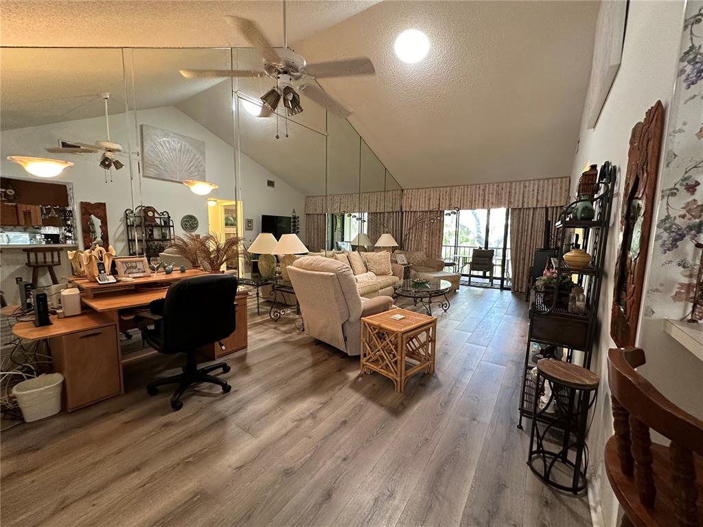 A living room with wood-look flooring, a mirrored wall, and a vaulted ceiling — 1647 BROOKHOUSE COURT UNIT 246, SARASOTA, FL