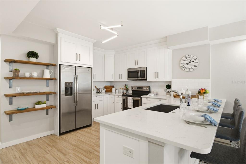 A modern kitchen features white cabinets, stainless steel appliances, an island, and open wood shelving — 4811 BAYSHORE BOULEVARD UNIT 303, TAMPA, FL