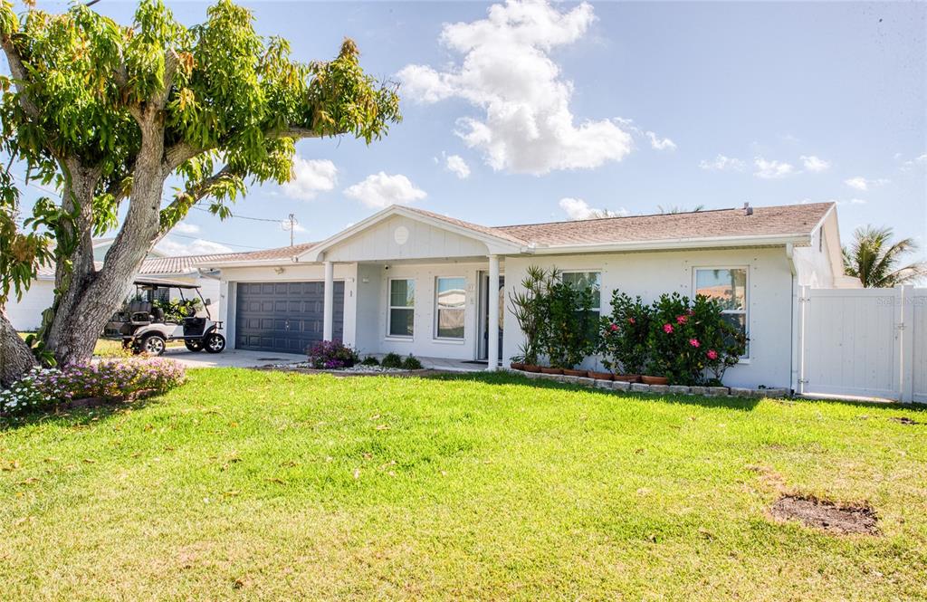 A single-story white house with a dark garage door, a front lawn, and a large tree — 551 CRYSTAL DRIVE, MADEIRA BEACH, FL