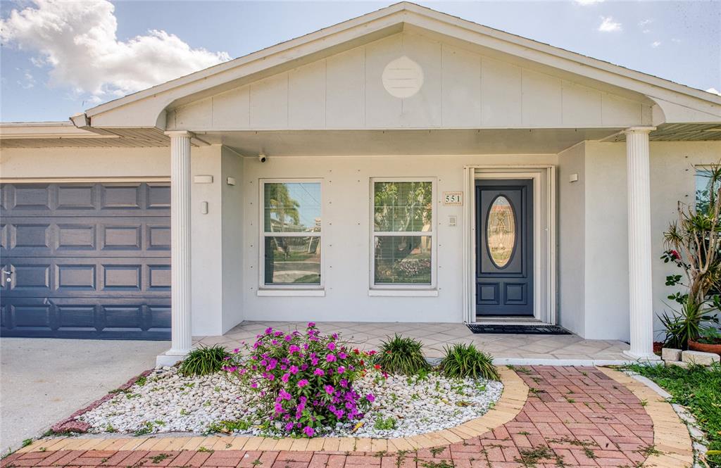 The exterior of a single-story house features a blue garage door, front door, and porch — 551 CRYSTAL DRIVE, MADEIRA BEACH, FL