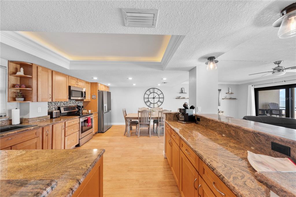 A kitchen with wood cabinets, granite countertops, and a dining area in an open layout — 4445 S ATLANTIC AVENUE UNIT 202, PONCE INLET, FL