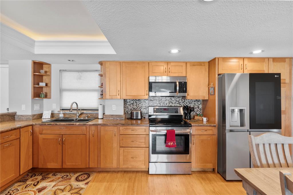 A kitchen features light wood cabinets, stainless steel appliances, a mosaic backsplash, and granite countertops — 4445 S ATLANTIC AVENUE UNIT 202, PONCE INLET, FL