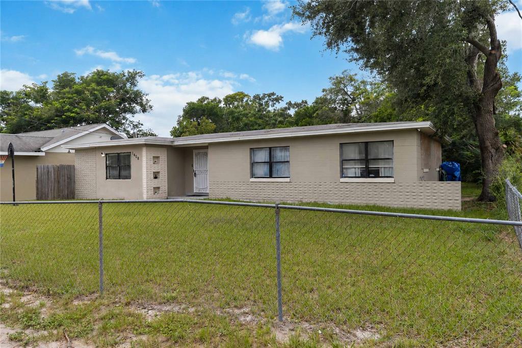 A single-story house with a beige exterior, a chain-link fence, and a large tree — 1408 ROGER BABSON ROAD, ORLANDO, FL