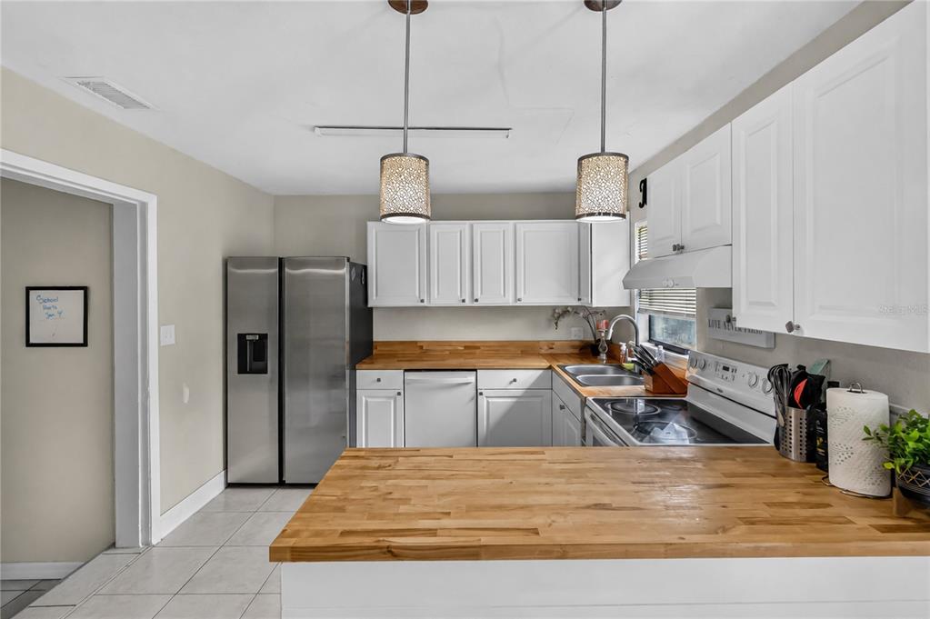 A kitchen features white cabinets, butcher block countertops, stainless steel appliances, and two pendant lights — 1408 ROGER BABSON ROAD, ORLANDO, FL