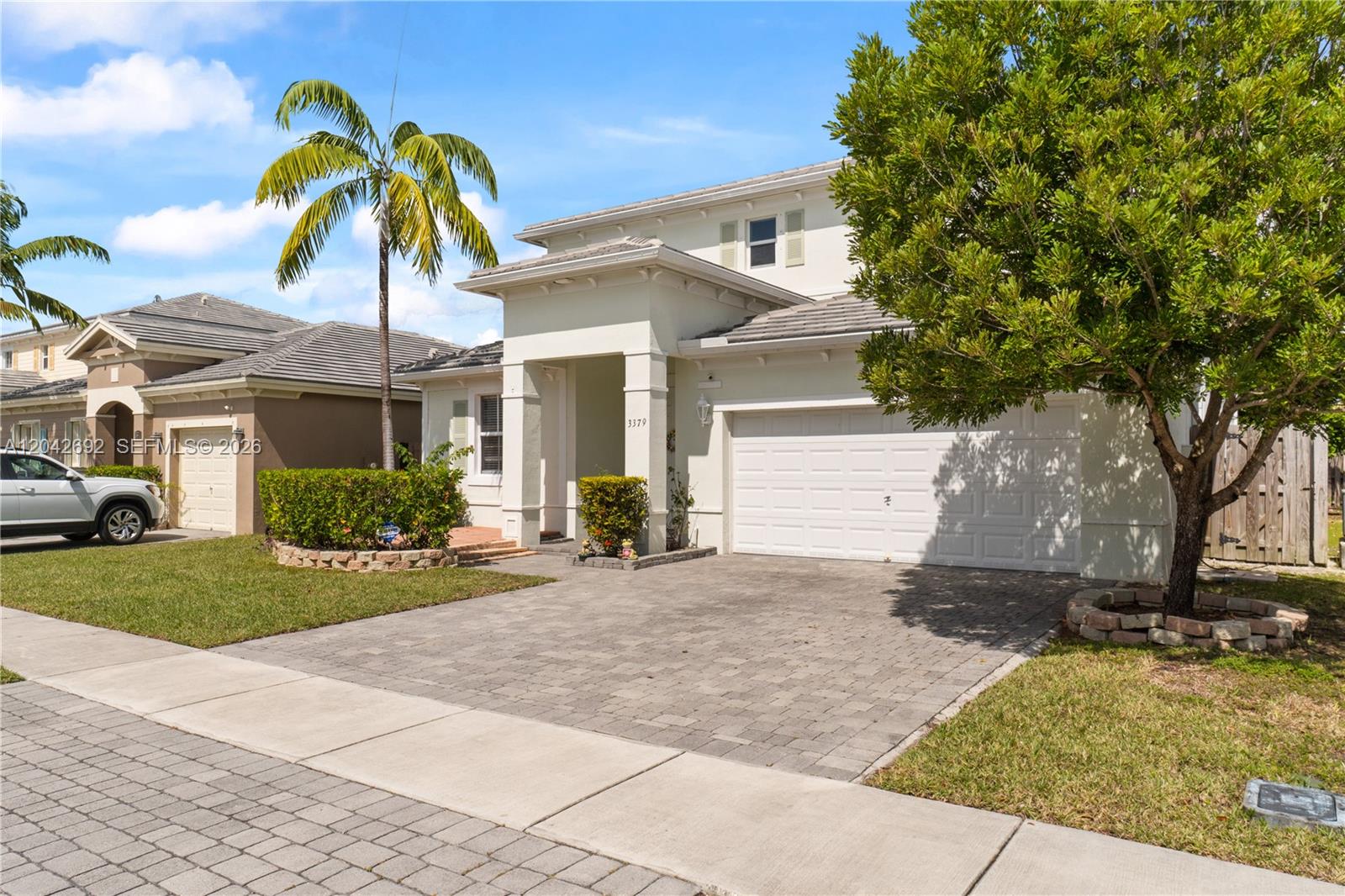 A two-story suburban house features a paved driveway, a white garage door, and landscaping — 3379 NE 1st St, Homestead FL 33033, HOMESTEAD, FL