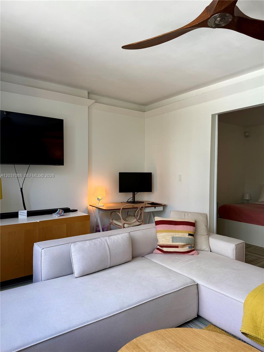 A living room features a sectional sofa, a wall-mounted television, and a small desk area — 2301 Collins Ave # 614, Miami Beach FL 33139, MIAMI BEACH, FL
