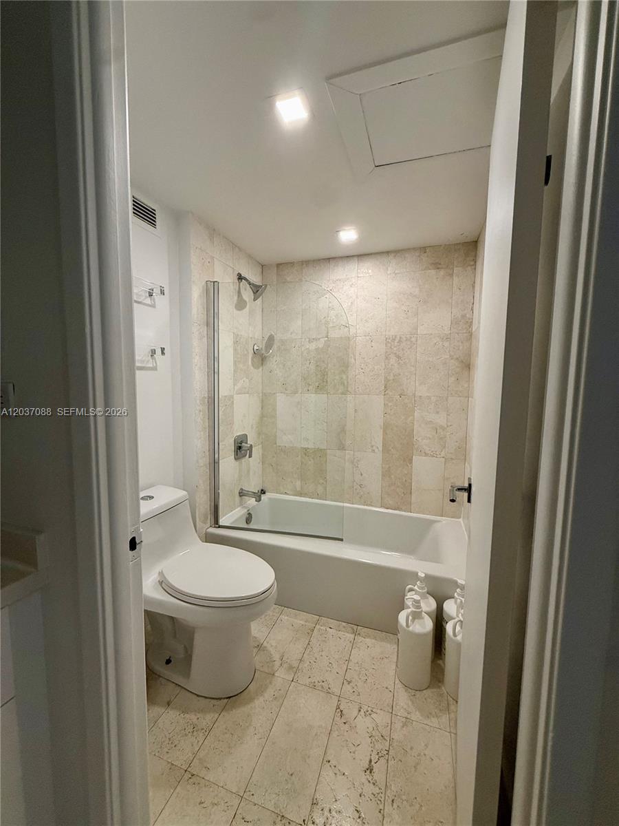 A bathroom features a toilet, a bathtub with a glass shower door, and tiled walls — 2301 Collins Ave # 614, Miami Beach FL 33139, MIAMI BEACH, FL