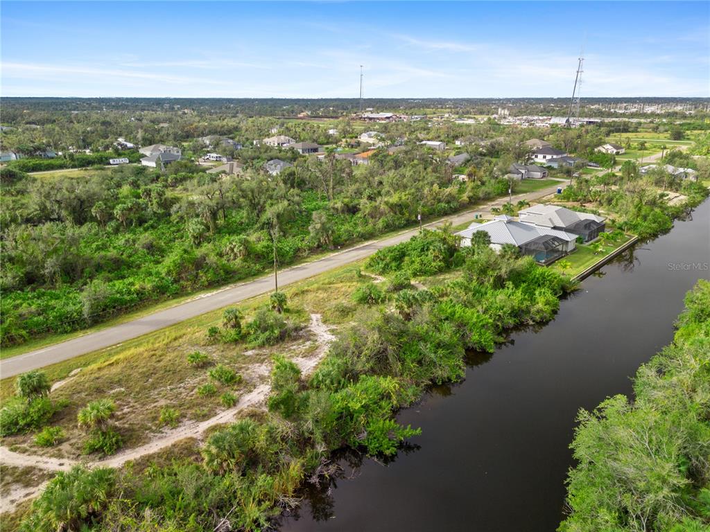 An aerial view shows a road running alongside a canal with nearby houses and vegetation — 13228 AMARYLLIS CIRCLE, PORT CHARLOTTE, FL