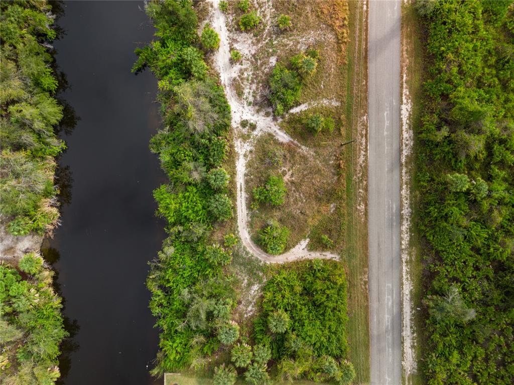An aerial view shows a vacant lot with a dirt path beside a canal and road — 13228 AMARYLLIS CIRCLE, PORT CHARLOTTE, FL
