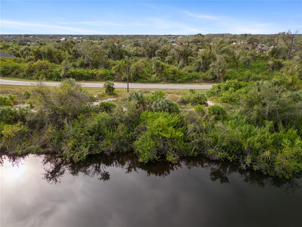 An aerial view shows a body of water in the foreground, a road, and dense vegetation — 13228 AMARYLLIS CIRCLE, PORT CHARLOTTE, FL