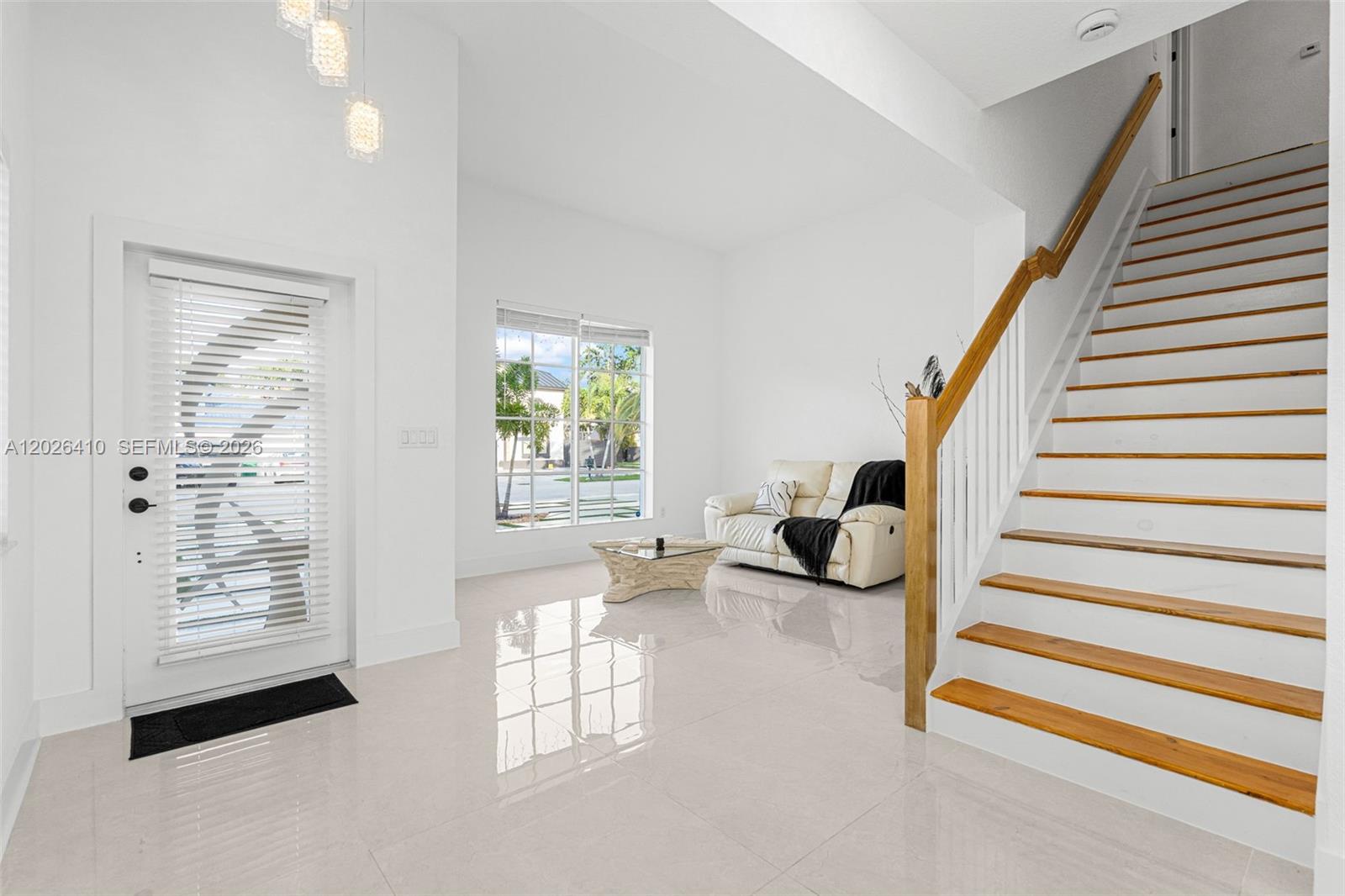 A bright entryway features white tile floors, a staircase with wooden treads, and a sofa — 1680 SW 154th Path, Miami FL 33185, MIAMI, FL