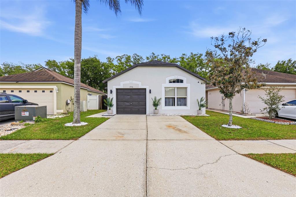 A single-story house with a gray garage, white stucco exterior, and a concrete driveway — 5916 LAKE FRONT DRIVE, WESLEY CHAPEL, FL