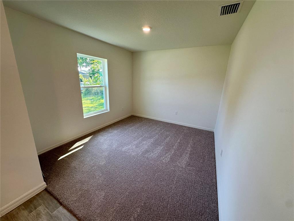 An empty bedroom with beige carpet, white walls, a single window, and a ceiling light — 12 ROYAL LEAF LANE, PALM COAST, FL