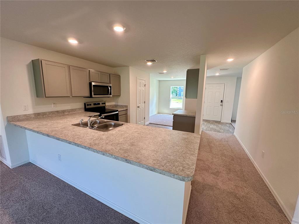 A kitchen with light-colored cabinets and a laminate countertop overlooks a carpeted living area — 12 ROYAL LEAF LANE, PALM COAST, FL