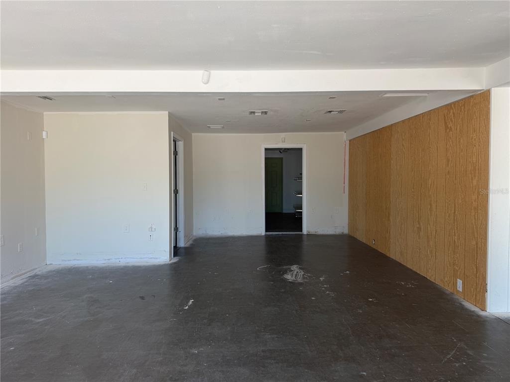 An unfinished room features dark concrete flooring, light-colored walls, and a wood-paneled accent wall — 1771 CLEARWATER LARGO ROAD, CLEARWATER, FL