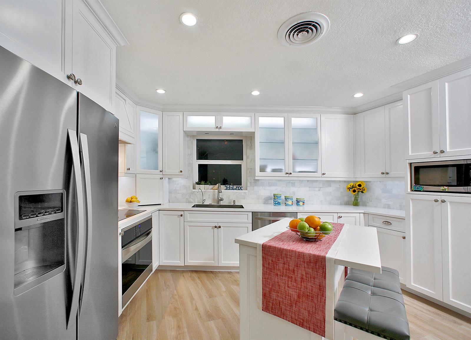 A bright kitchen features white cabinetry, stainless steel appliances, a center island, and wood flooring — 5501 N Ocean Boulevard, Ocean Ridge FL 33435, OCEAN RIDGE, FL