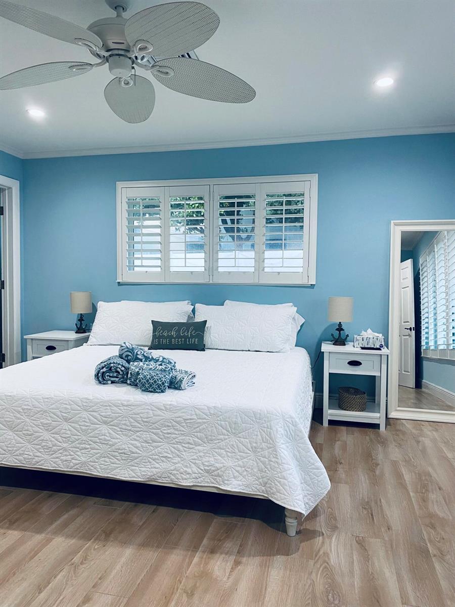 A bedroom features light blue walls, a white bed with patterned pillows, and wood-look flooring — 5501 N Ocean Boulevard, Ocean Ridge FL 33435, OCEAN RIDGE, FL