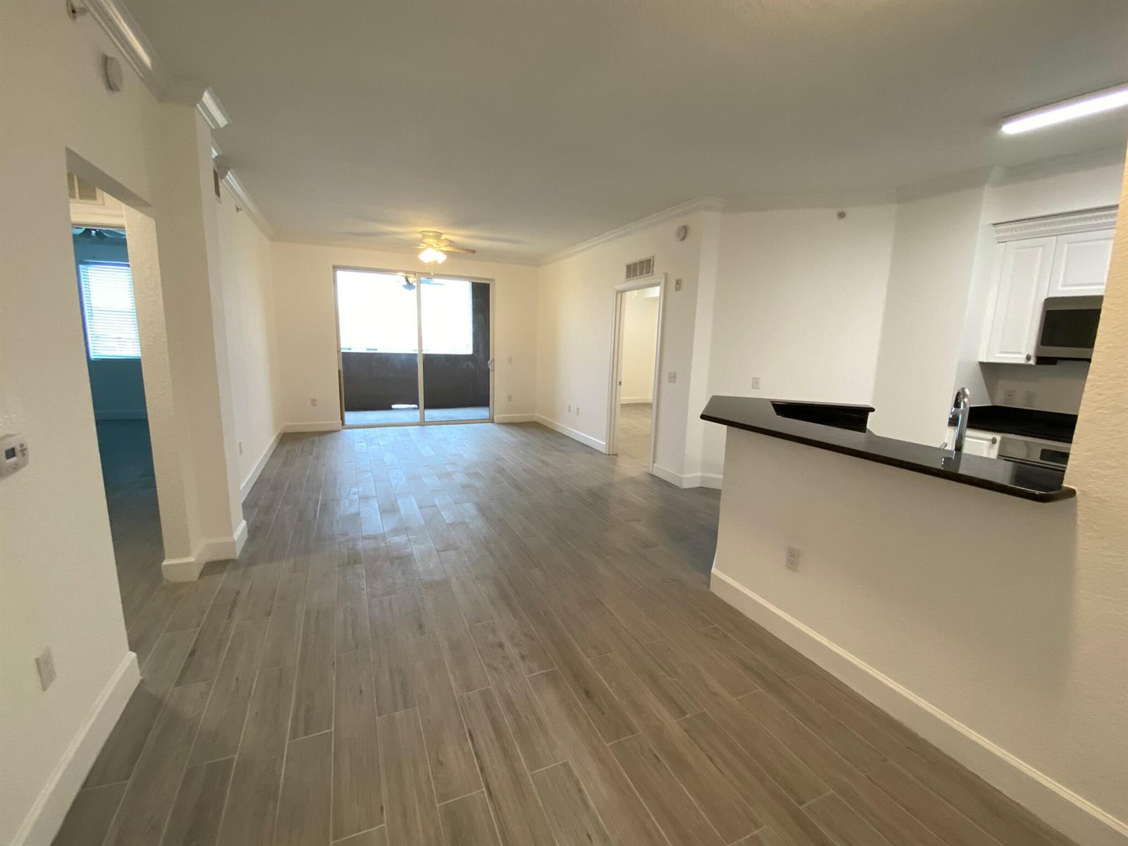 An open-concept living area features wood-look tile flooring, a kitchen breakfast bar, and balcony access — 1690 Renaissance Commons Boulevard # 1418, Boynton Beach FL 33426, BOYNTON BEACH, FL