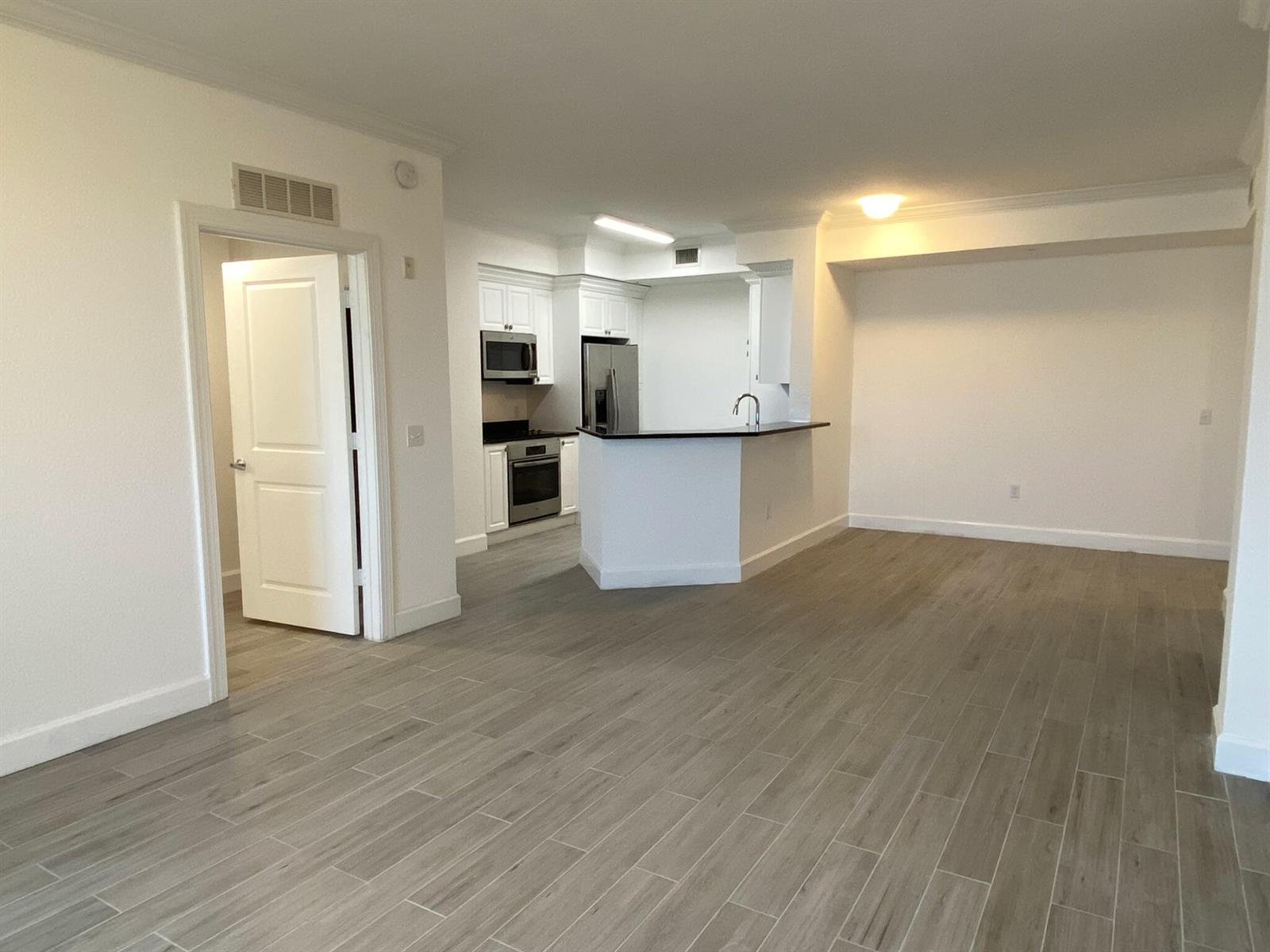 An open-concept living area features light wood-look tile flooring and a kitchen with white cabinets — 1690 Renaissance Commons Boulevard # 1418, Boynton Beach FL 33426, BOYNTON BEACH, FL