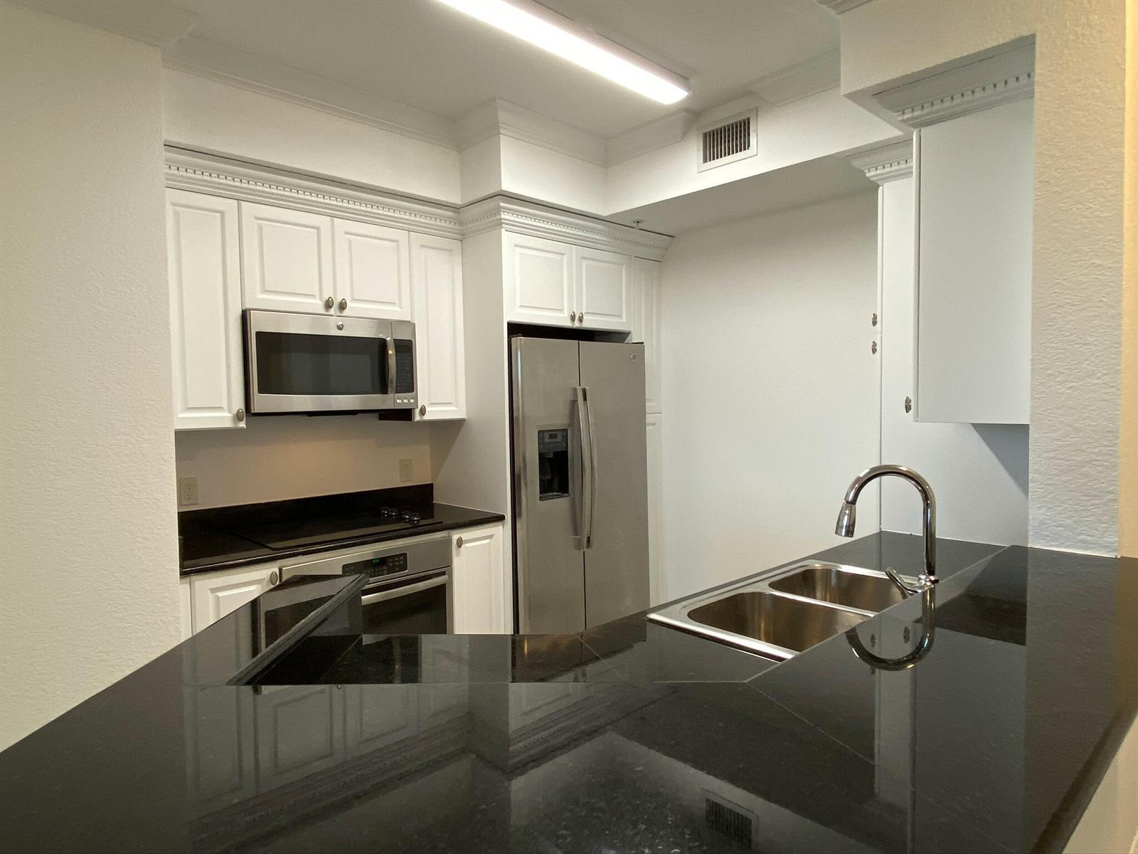 A kitchen features white cabinets, stainless steel appliances, and black granite countertops — 1690 Renaissance Commons Boulevard # 1418, Boynton Beach FL 33426, BOYNTON BEACH, FL